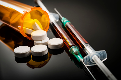 prescription pill falling out of a pill bottle laying next to syringes