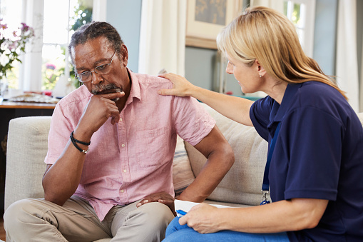 A depressed man sitting on a couch is being offered support by a friend.