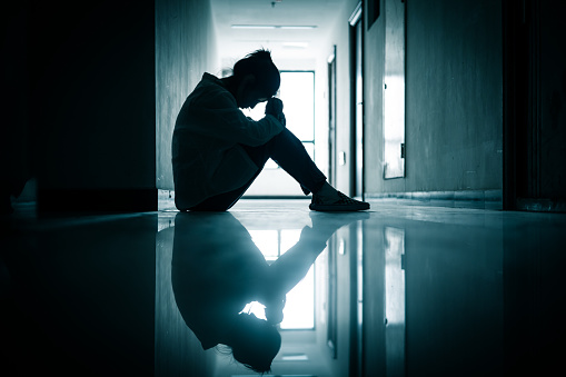 Silhouette of a depressed teenage girl sitting in a hallway 