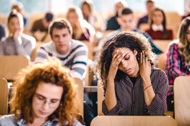 College students in a large classroom show signs of stress - student with hand on forehead looking down