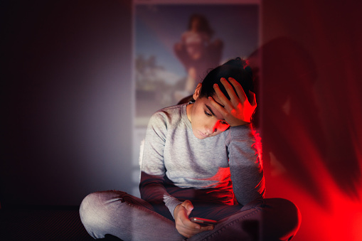 A 13-year-old girl is using her smartphone in the dark room. The content she is browsing projects in front of her.