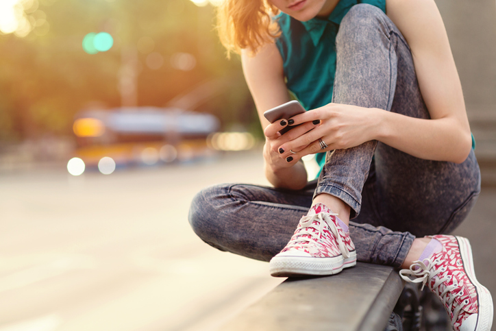 teen girl sitting on bridge on cell phone near sunset
