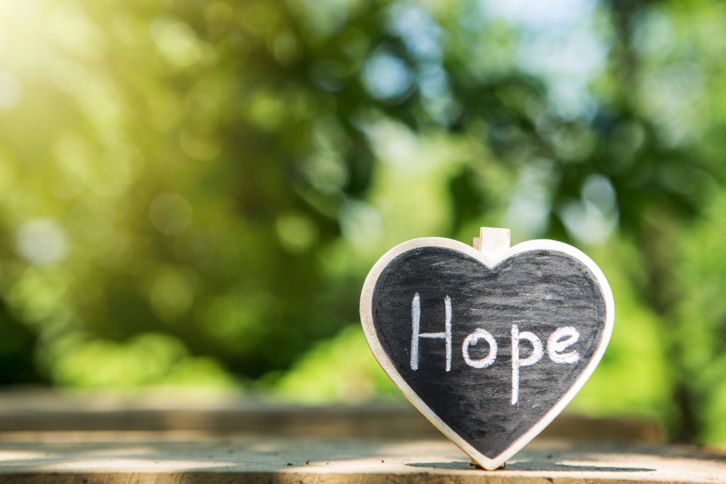 The word "hope" inscribed on a heart shape against a green outdoor background.