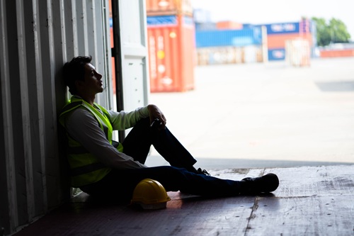 An upset male worker sitting alone in a dark storage container.